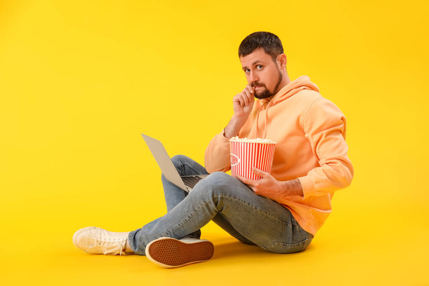 Handsome man with laptop biting nails on yellow background - Foto, afbeelding