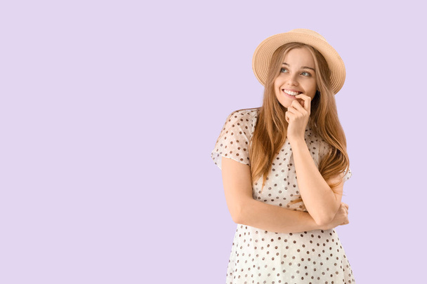 Young woman in hat biting nails on lilac background - Foto, immagini