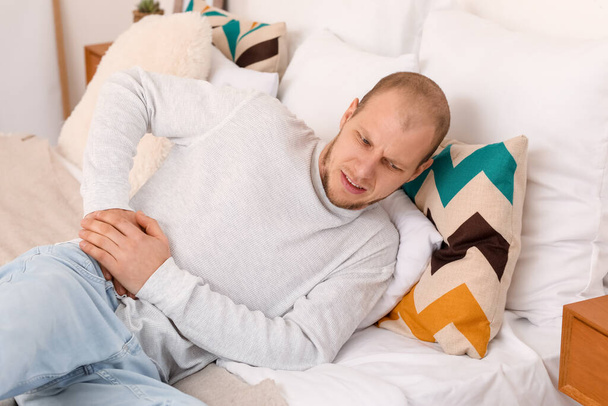 Young man with appendicitis lying on bed at home - Foto, Bild