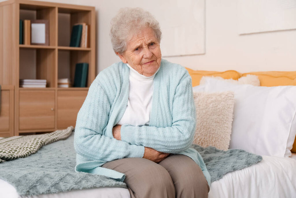 Старшая женщина с аппендицитом сидит в спальне - Фото, изображение