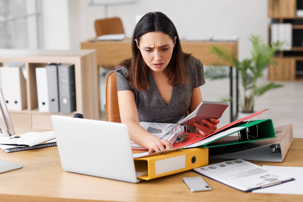 Femme comptable stressée travaillant avec des documents et une calculatrice à la table au bureau - Photo, image