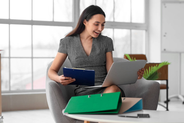 Female accountant with laptop and clipboard sitting in office - Photo, Image