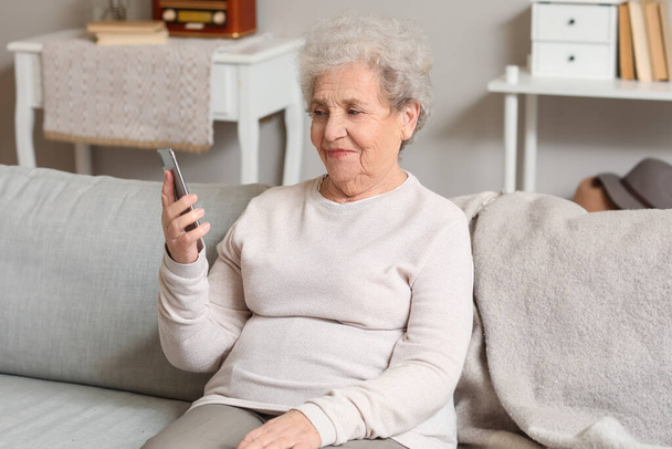 Senior žena s mobilním telefonem video chatování na pohovce doma - Fotografie, Obrázek