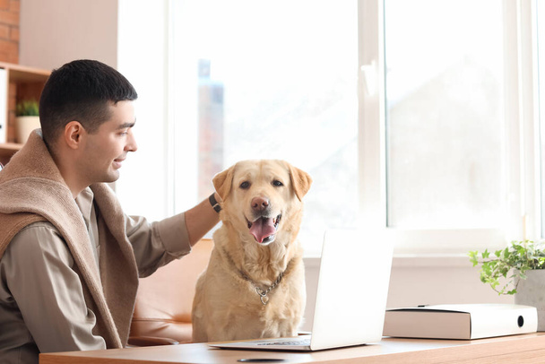 Mladý muž s roztomilou labradorský pes u stolu v kanceláři - Fotografie, Obrázek