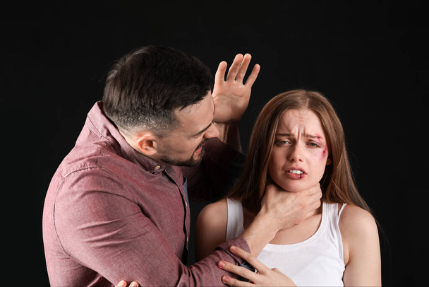 Angry young man holding his bruised wife by throat on dark background. Domestic violence concept - Foto, Imagem