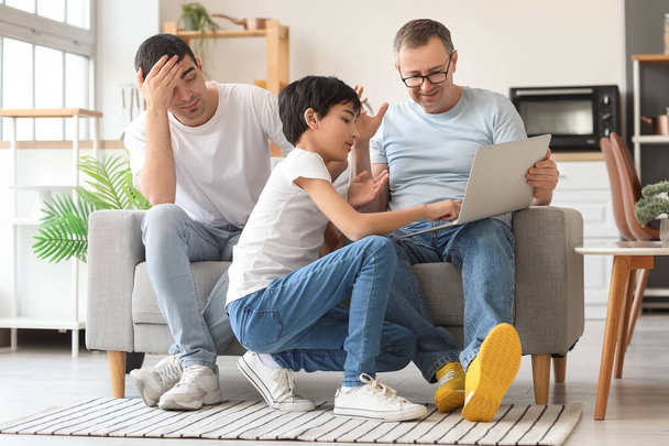 Happy little boy with his dad and grandfather using laptop at home - Photo, Image