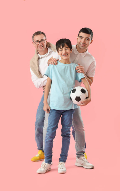 Счастливый маленький мальчик с отцом и дедушкой держит футбольный мяч на розовом фоне - Фото, изображение