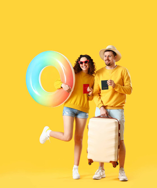 Молодая пара с паспортами, надувным кольцом и чемоданом на желтом фоне - Фото, изображение