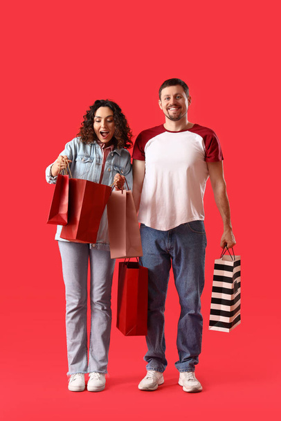 Young couple with shopping bags on red background - Photo, Image