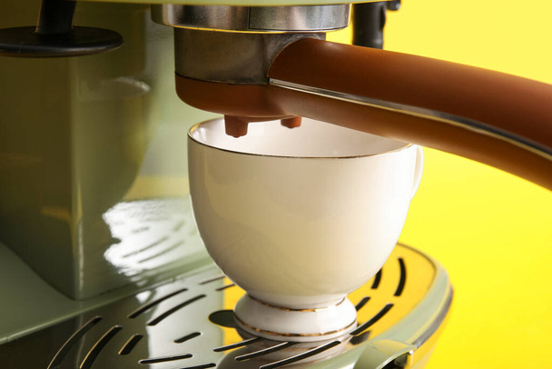Moderní kávovar s šálkem na žlutém pozadí, detailní záběr - Fotografie, Obrázek
