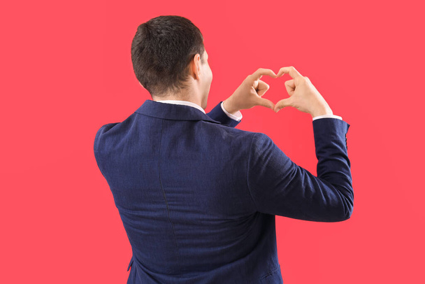 Young man making heart with his hands on red background, back view - Foto, Imagen