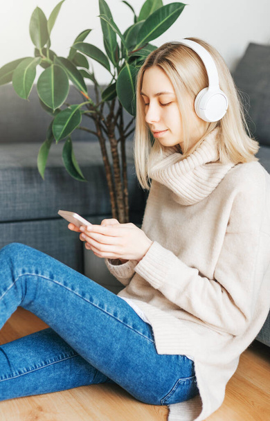 Jeune femme blonde dans un casque écoutant de la musique et se relaxant à la maison. - Photo, image