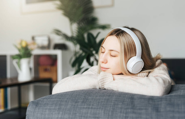 Young blonde woman in headphones listening to music and relaxing at home. - Foto, immagini