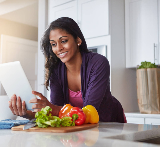 Loaded with recipes for a healthy lunch. a young woman using a digital tablet while preparing a healthy meal at home - 写真・画像