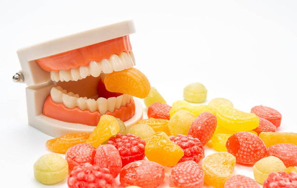 Una variedad de caramelos de colores sobre un fondo blanco, con un modelo de dientes mordiendo uno de los caramelos - Foto, imagen