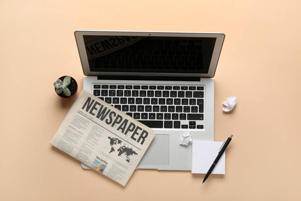 Laptop with newspaper, pen and sticky notes on beige background - Photo, Image