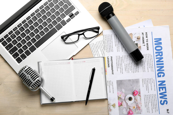 Laptop com óculos, microfones, notebook e jornais sobre fundo de madeira claro - Foto, Imagem