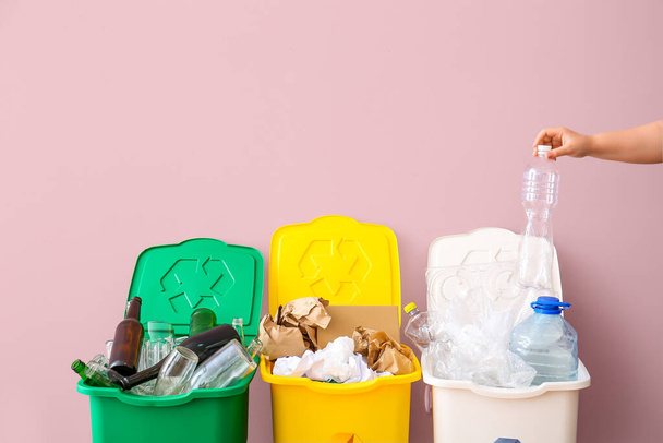 Vrouw gooit vuilnis in vuilnisbak bij roze muur. Recycling concept - Foto, afbeelding
