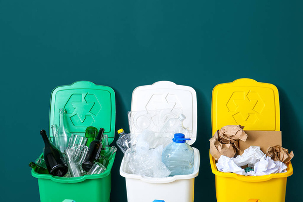 Pattumiere con simbolo di riciclaggio e diverse immondizie vicino alla parete verde - Foto, immagini