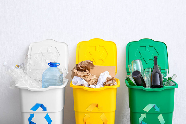 Trash bins with recycling symbol and different garbage near white wall - 写真・画像