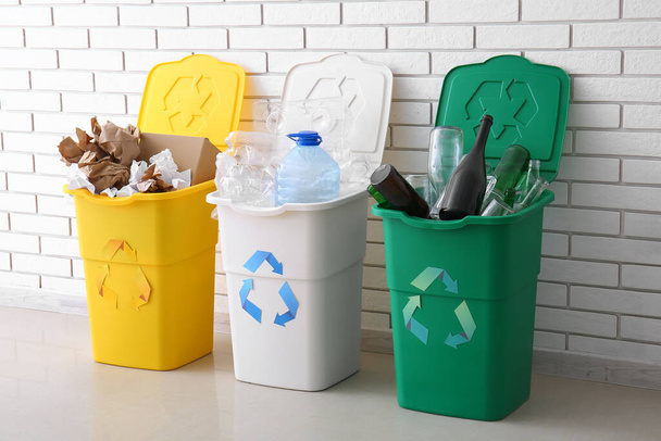 Papeleras con símbolo de reciclaje y diferentes basura cerca de la pared de ladrillo blanco - Foto, Imagen