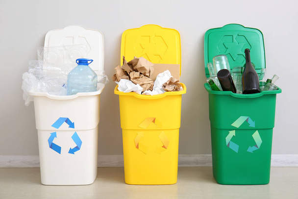Poubelles avec symbole de recyclage et différentes ordures près du mur blanc - Photo, image