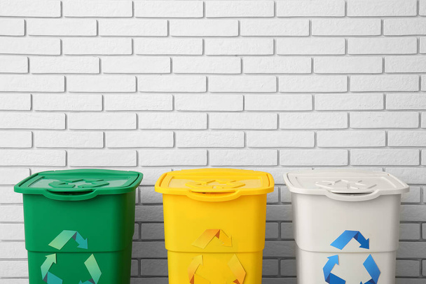 Diferentes lixeiras com símbolo de reciclagem perto da parede de tijolo branco - Foto, Imagem