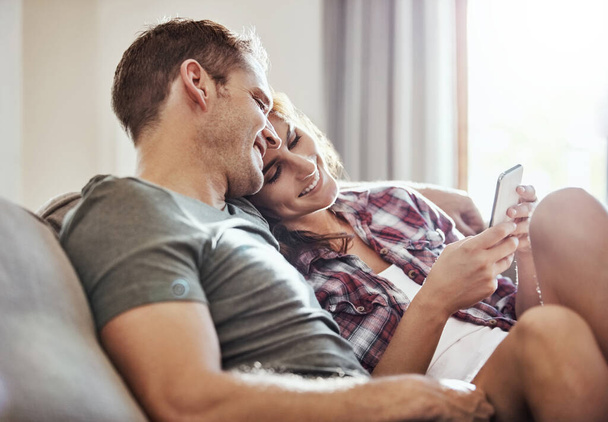 La felicità è poter condividere ciò che ami. una giovane coppia si rilassa sul divano insieme e utilizzando un telefono cellulare - Foto, immagini