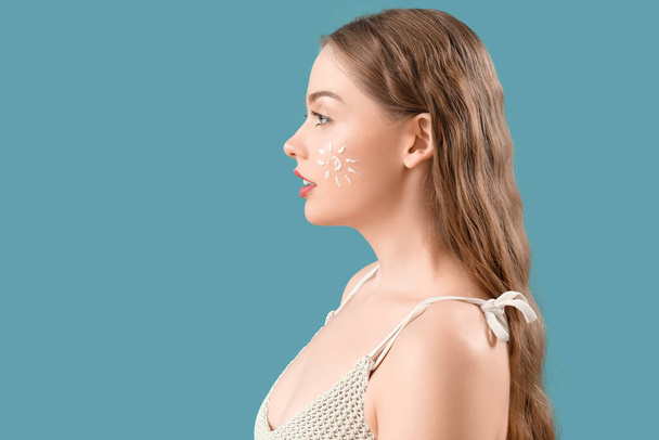 Beautiful young woman with sunscreen cream on her face against blue background - Φωτογραφία, εικόνα