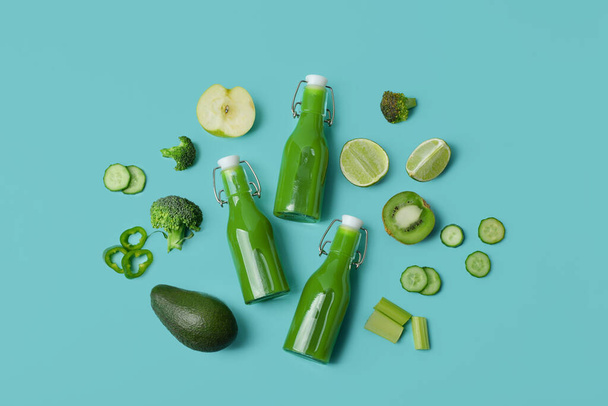 Üvegek ízletes zöld lé és összetevők türkiz háttér - Fotó, kép