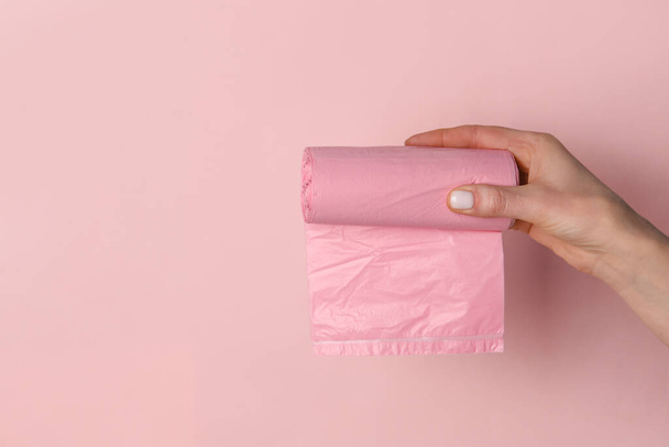 Female hand holding roll of garbage bags on pink background - Fotoğraf, Görsel