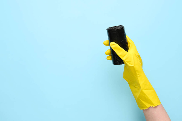 Hand in rubber handschoen met rol vuilniszakken op blauwe achtergrond - Foto, afbeelding