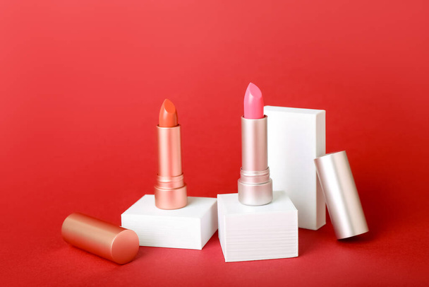 Decorative plaster podiums and lipsticks on red background - Photo, image