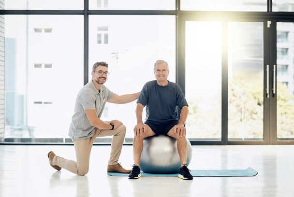 Fare progressi ad un ritmo confortevole. un fisioterapista premuroso che aiuta il suo paziente maturo a usare una palla da yoga in un centro di riabilitazione - Foto, immagini