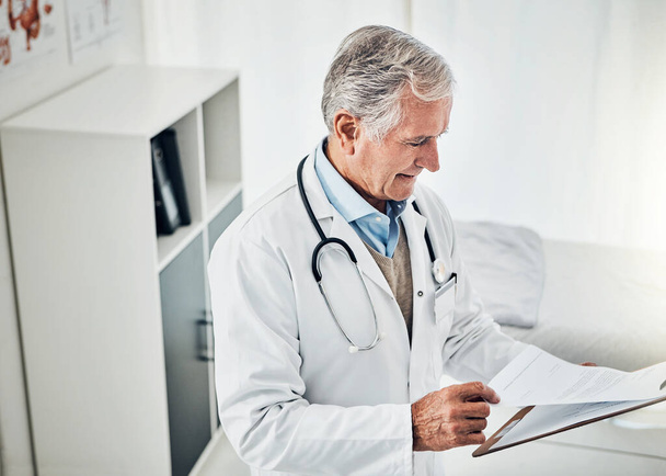 Хесус все ще найкращий у своїй галузі. зрілий лікар читає пацієнтський файл, стоячи у своїй консультаційній кімнаті
 - Фото, зображення