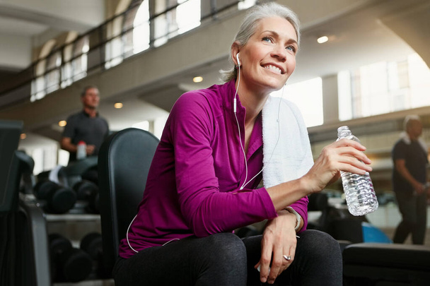 Štěstí je důležité pro velké zdraví. Portrét šťastné starší ženy držící láhev s vodou a dává si pauzu od cvičení v tělocvičně - Fotografie, Obrázek