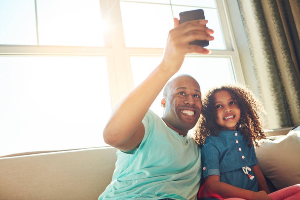 Wyślij to zdjęcie mamusi. szczęśliwy ojciec i jego mała dziewczynka pozowanie do selfie razem na kanapie w domu - Zdjęcie, obraz