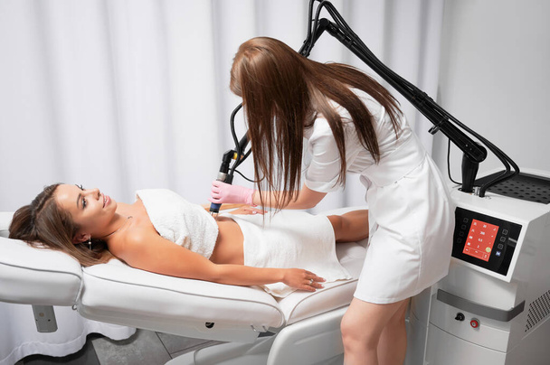 Beautician performing laser resurfacing of abdomen, ridding patient of stretched skin. Fractional CO2 laser is modern device for treatment of skin defects, scars and stretch marks after childbirth. - Fotoğraf, Görsel