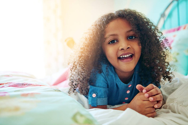 I love my big, comfy bed. Portrait of a cheerful little girl relaxing on her bed at home - Fotografie, Obrázek