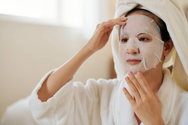 Jeune femme vietnamienne appliquant un masque en feuille pour revitaliser la peau terne - Photo, image