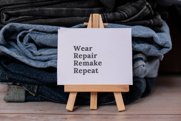 WEAR REPAIR REMAKE REPEAT text na papíře poznámka na džíny oblečení sortiment z druhé ruky udržitelné nakupování. Minimální skříň na kapsle. Udržitelná módní nadměrná spotřeba, vědomá spotřeba - Fotografie, Obrázek