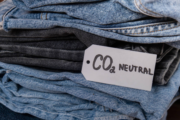CO2-neutraler Text auf einem Stapel Jeans. Umweltfreundlichkeit, Klimawandel, grüner Treibstoff und Erdschutzkonzept. Recyclingetikett für CO2-Emissionspapiere. Natürliche Bio-Jeans-Kleidung - Foto, Bild