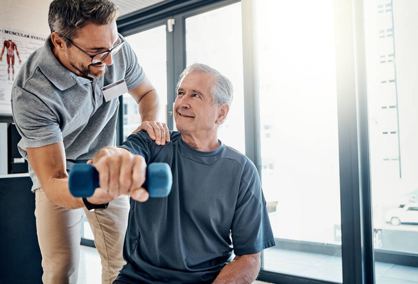 Im really impressed by your progress. a friendly physiotherapist helping his mature patient to use dumbbells in a rehabilitation center - Fotoğraf, Görsel