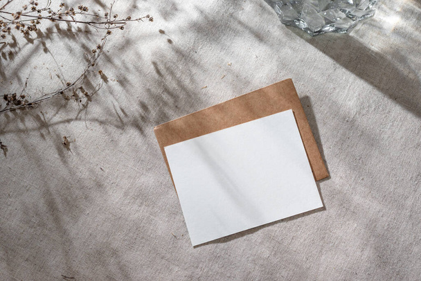 Prázdná papírová karta s maketou kopírovacího prostoru a obálkou na béžovém lněném pozadí s estetickými stíny slunečního světla, pozvánkou nebo šablonou blahopřání - Fotografie, Obrázek