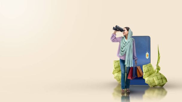 Asian Muslim woman in a headscarf looking through binoculars while holding shopping bags on a colored background - Fotografie, Obrázek