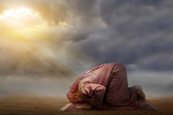 Muslim man with a beard wearing keffiyeh with agal in praying position (salat) on the prayer rug with the sunset scene background - Foto, imagen