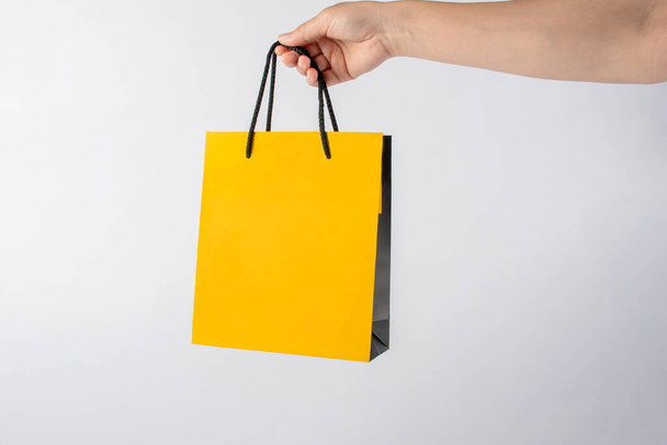 白い背景に隔離されたショッピングのための手に黄色の紙袋 - 写真・画像