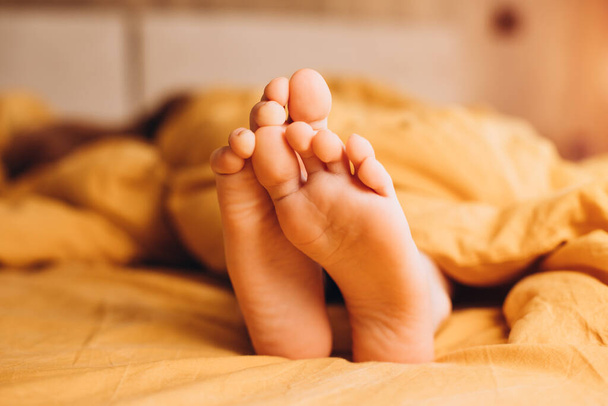 Acercamiento de las piernas de un niño asomándose de una cama amarilla con un caniche rojo en el fondo. Vista frontal - Foto, imagen