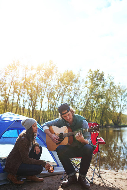 Csináljunk Smore-ból emlékeket. Egy fiatalember játszik a barátnőjének egy dalt a gitárján, miközben kempingezik. - Fotó, kép