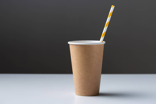 Disposable cardboard biodegradable cup on a white table with a straw. - Photo, image